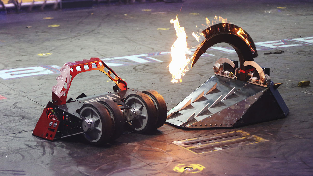 small roomba robots with spikes and flames fighting in an arena