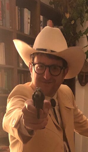 Brace Belden wearing a cowboy hat wielding a mighty gun at the camera