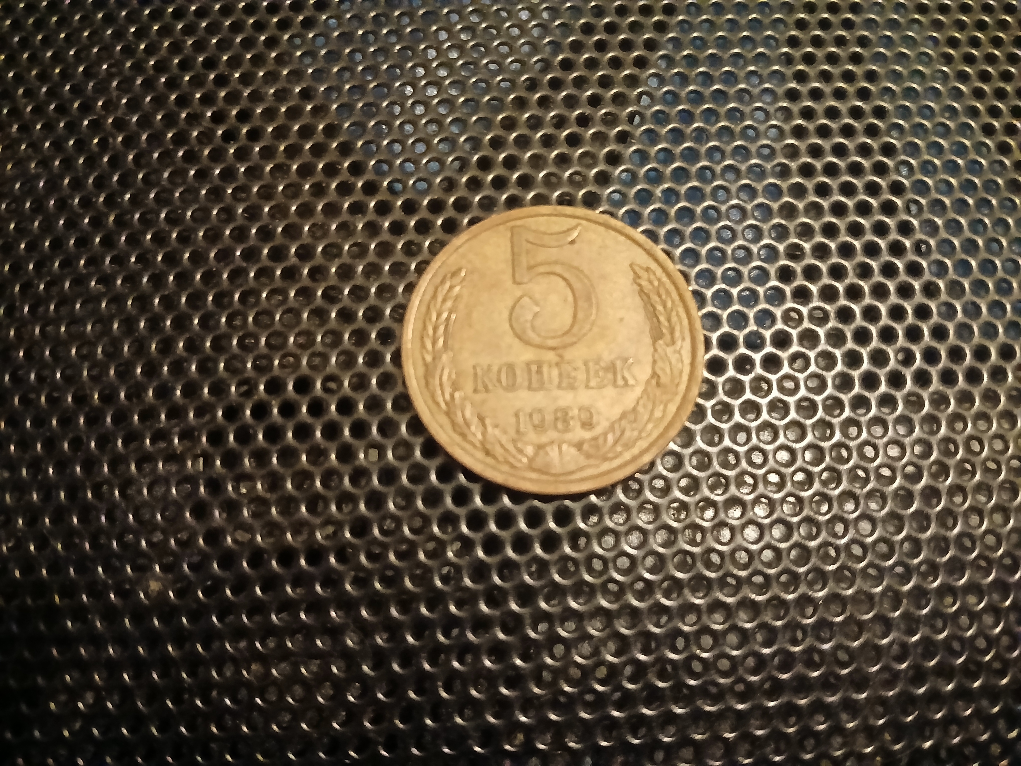 Obverse side of the same Soviet 5 kopek coin. It has a large numeral 5, beneath it the word "kopeyek" written in Cyrillic, beneath that in turn the numerals 1989. This lettering is surrounded by a wreath of wheat.