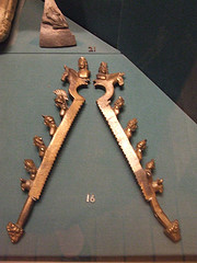 Picture shows two large bronze clamps laying side-by-side. They have grooves on the inside to provide greater grip. The outside edge of the clamps is deckrated with the heads of mythological figures, bulls, and horses