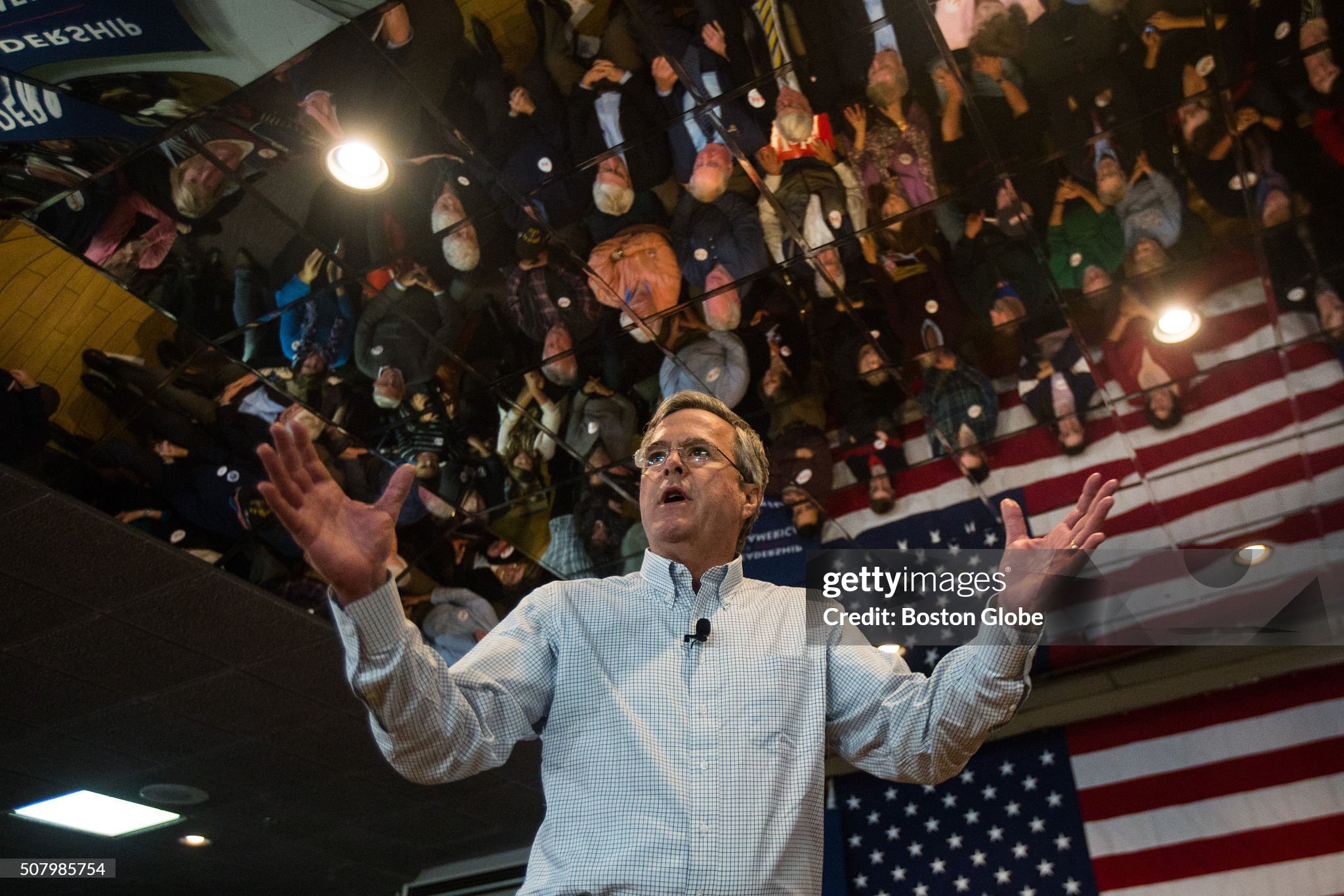 John Ellis "Jeb!" Bush, extending his arms out to his sides. They are not yet extended far enough to hug the entire map of the United States of America, but it happens later in this same photo shoot.